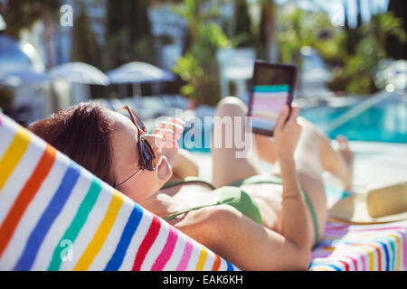 Smiling woman with digital tablet sunbathing by swimming pool Stock Photo