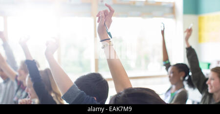 Teenage students with arms raised in classroom Stock Photo