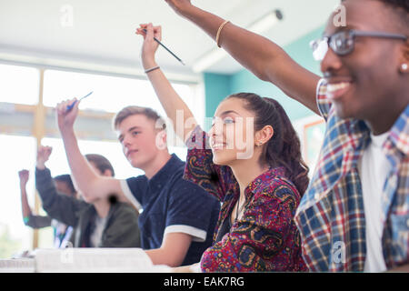 Students sitting in classroom during lesson, smiling and raising hands Stock Photo