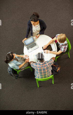 Overhead view of student doing homework at round table, using laptop and digital tablet Stock Photo