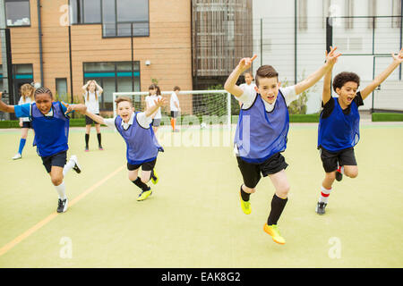 Schoolboys wearing sport uniforms running with arms raised in soccer field in front of school