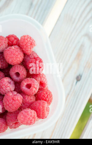 Close up of ripe raspberries in plastic box on garden table. Stock Photo