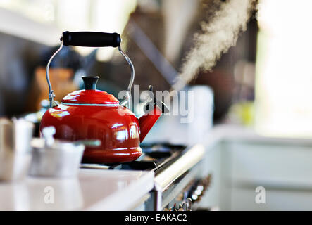 Red old fashion kettle on cooker with steam coming out Stock Photo