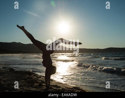 Young woman doing gymnastics on the beach, backlight, Corsica, France Stock Photo