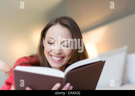 Smiling woman reading book in bedroom Stock Photo