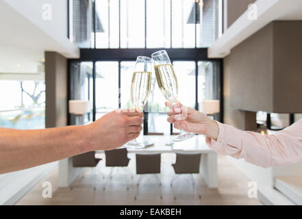 Hands of couple raising toast with champagne flutes in modern dining room Stock Photo