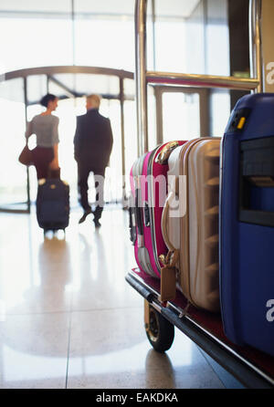 Rear view of man and woman leaving hotel lobby, suitcases on luggage cart in foreground Stock Photo