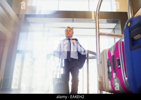 Low angle view of man entering hotel lobby, suitcases on luggage cart in foreground Stock Photo