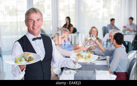 Portrait of waiter holding plate with fancy meals, people at restaurant tables in background Stock Photo