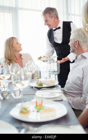 Waiter serving fancy dish to woman sitting at restaurant table Stock Photo