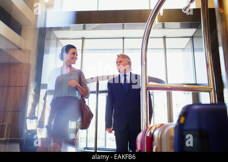Smiling man and woman entering hotel lobby, suitcases on luggage cart in foreground Stock Photo