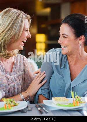 Two female friends talking and laughing in restaurant, fancy dishes on table