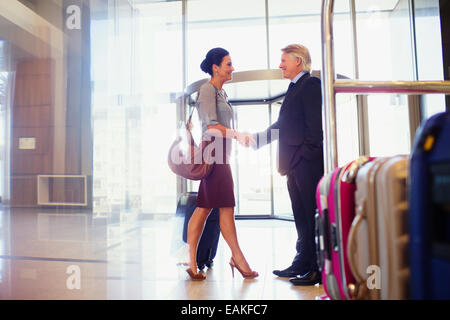 Man and woman shaking hands in hotel lobby, luggage cart in foreground Stock Photo