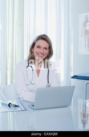 Portrait of smiling female doctor sitting at desk with laptop Stock Photo