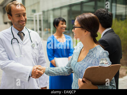 Smiling doctor shaking hand with woman in front of hospital Stock Photo