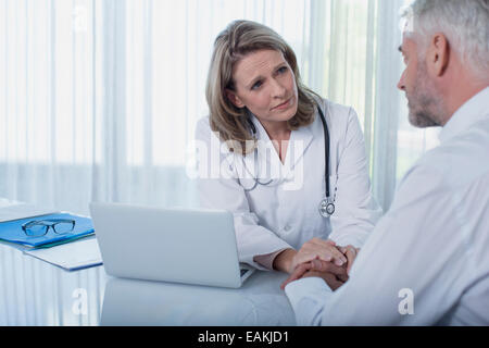 Female doctor sitting at desk with laptop and consoling patient Stock Photo