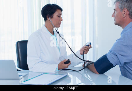 Female doctor taking patient's blood pressure in office Stock Photo