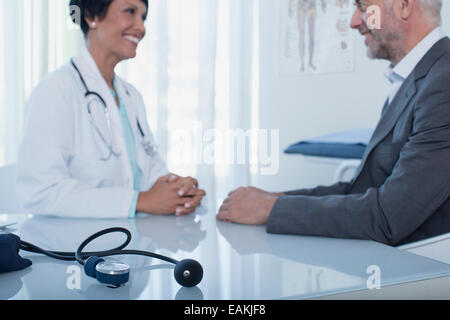 Smiling female doctor talking to patient at desk in office, blood pressure gauge in foreground Stock Photo