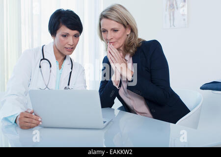 Female doctor and patient using laptop in hospital office