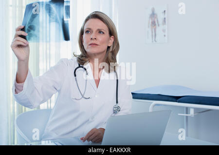 Female doctor looking at x-ray at desk with laptop in office Stock Photo