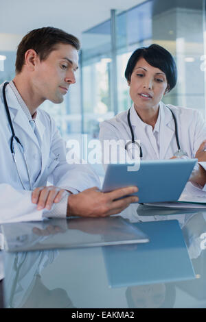 Doctors discussing patient's treatment at desk, using digital tablet Stock Photo