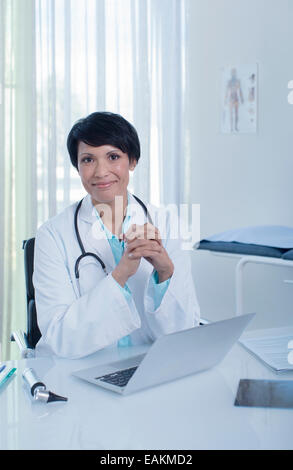 Portrait of smiling female doctor sitting at desk with laptop in office Stock Photo