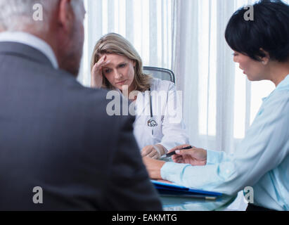 Female doctor, man and woman talking at table in conference room Stock Photo