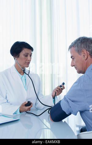 Female doctor taking patient's blood pressure at desk in office Stock Photo