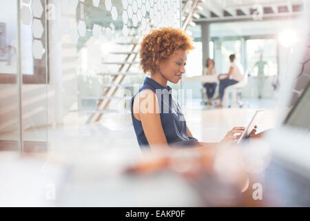 Woman using digital tablet in office, colleagues in background Stock Photo