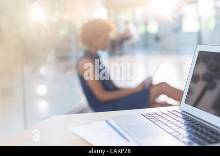 Open laptop on desk, woman in background Stock Photo