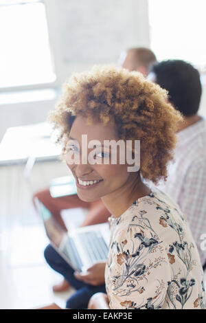 Portrait of smiling young woman in office, colleagues in background Stock Photo
