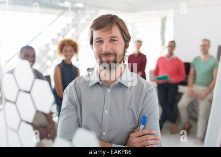 Portrait of smiling businessman wearing gray shirt, office team in background Stock Photo