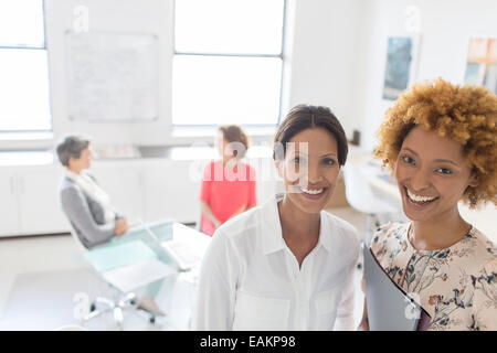 Portrait of two smiling business women in office, colleagues talking in background Stock Photo