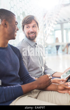 Two smiling men talking, holding digital tablet in office corridor Stock Photo