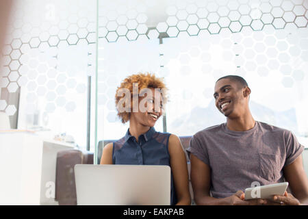 Woman using laptop and man using tablet smiling, looking at each other Stock Photo