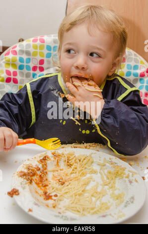 A little boy (ca. 2 years old) eats a plate of spaghetti and tomato sauce. Stock Photo