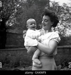 1940s, historical picture showing a delighted mother outside in a garden holding her smiling baby in a wollen outfit with cardigan. Stock Photo
