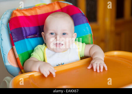 Adorable baby eating in high chair. Baby's first solid food Stock Photo