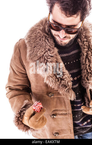 a young man wearing a sheepskin coat and holding a very small christmas gift. Isolated over white Stock Photo