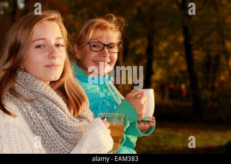 Daughter and mother drink tea in autumn park, horizontal Stock Photo