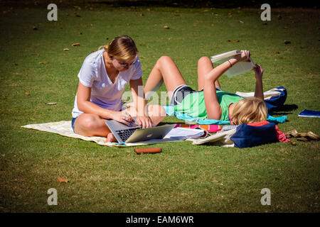 Two female students reading and using laptop computer relax on the grass on the campus at Vanderbilt University, Nashville, TN Stock Photo