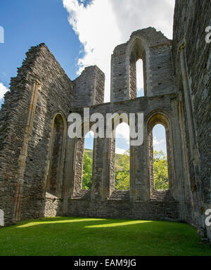 High stone walls of 13th century Valle Crusis abbey ruins rising from emerald grass to blue sky near Llantysilio in Wales Stock Photo