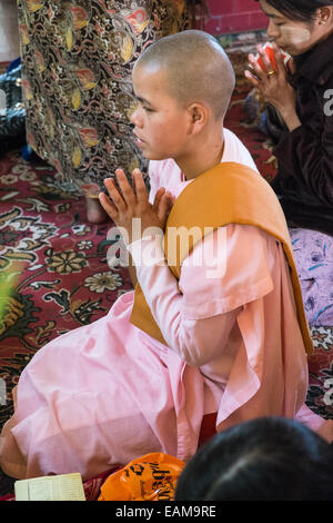 Woman nun devotee praying huge golden Buddha, Mahamuni statue one of the most revered Buddhas in Burma.Mandalay, Burma,Myanmar. Stock Photo