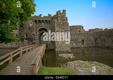 Impressive entrance & wooden bridge over moat at well preserved ruins of historic Beaumaris castle under blue sky in Wales Stock Photo