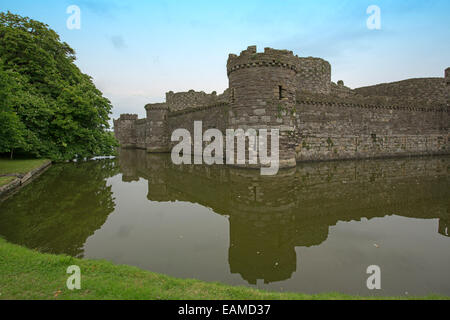 Spectacular 13th century Beaumaris castle  with high walls & towers reflected in calm water of moat under blue sky in Wales Stock Photo