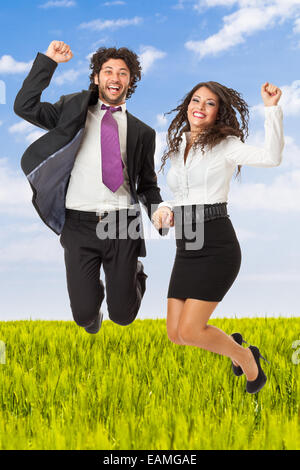 An handsome businessman and a gorgeous businesswoman jumping over green meadow Stock Photo