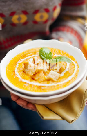 Woman holding pumpkin soup with croutons, cream and basil Stock Photo