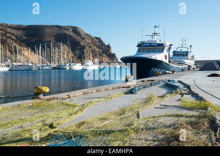 Fishing nets drying in the sun on the quay and fishing boats moored at Javea harbour Spain Stock Photo