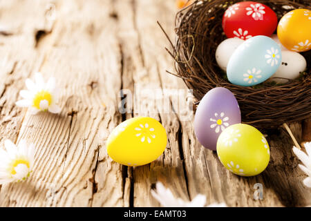 Easter eggs in nest with chamomiles blossoms, placed on wooden table Stock Photo