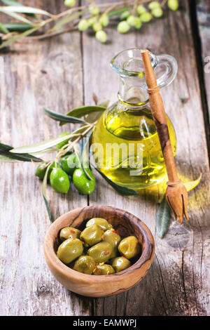 Green olives in olive wood bowl and bottle of olive oil served on old wooden table Stock Photo